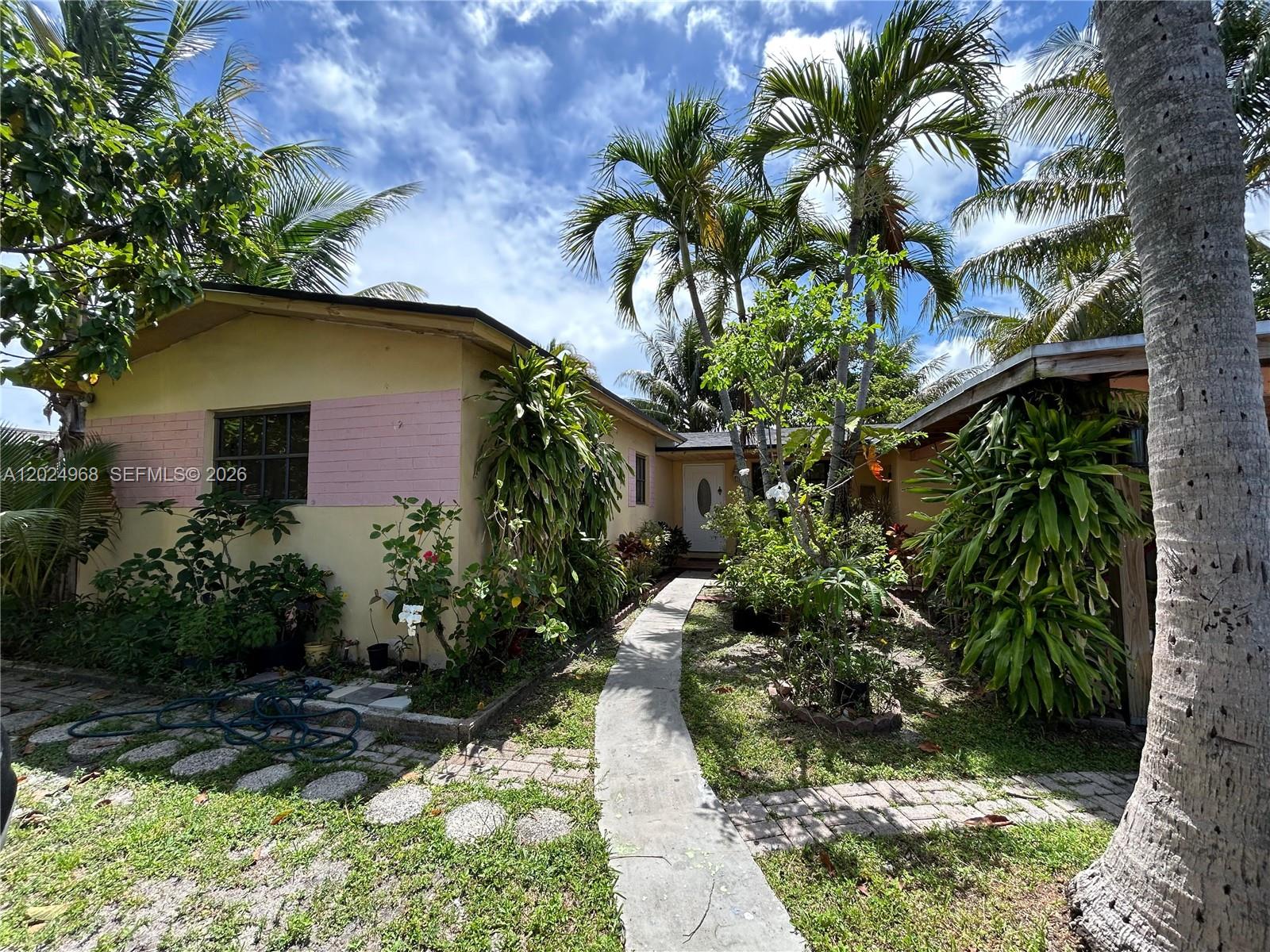 A concrete walkway leads to the front entrance of a yellow house with palm trees — 3650 SW 39th Ave, West Park FL 33023, WEST PARK, FL