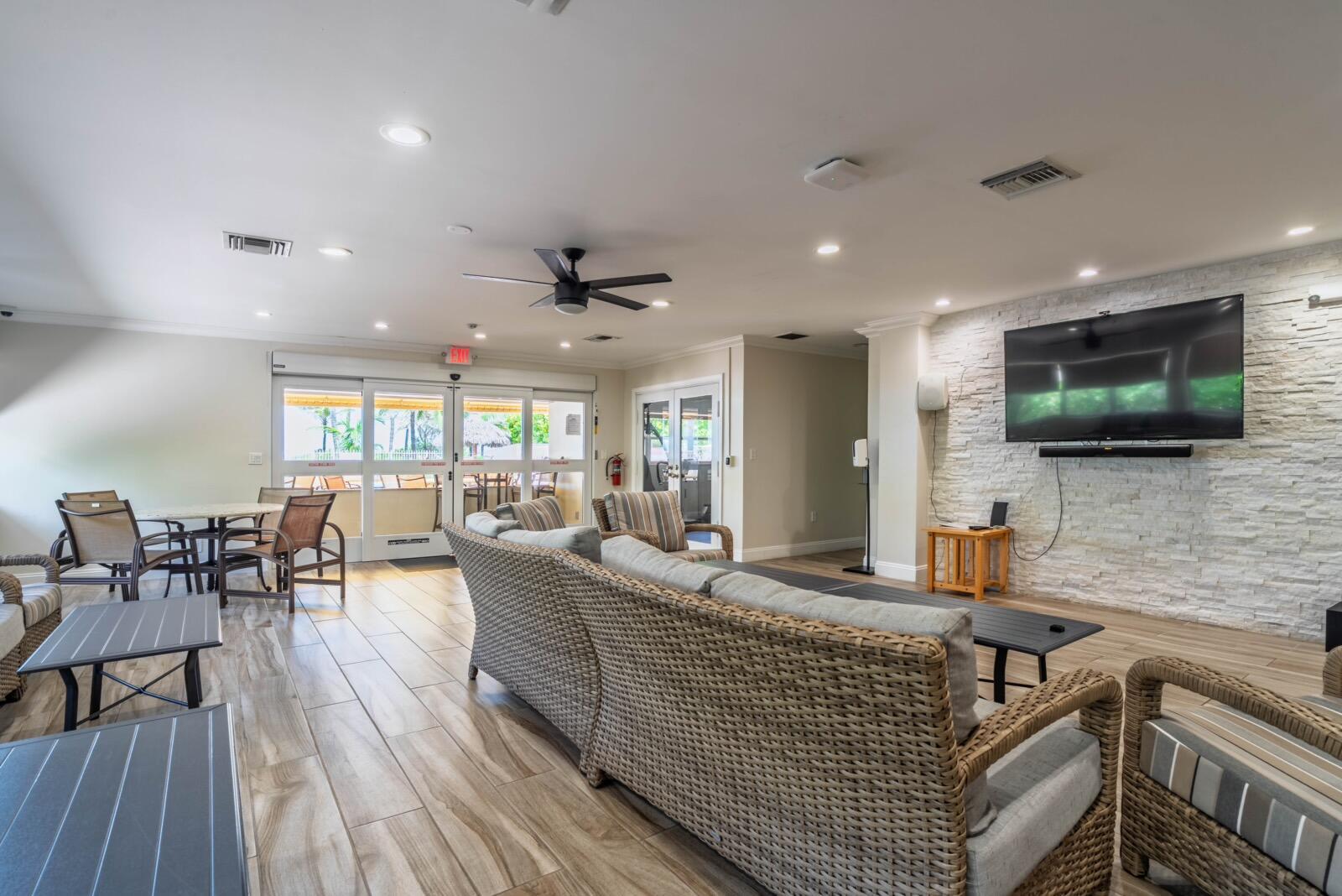 A lounge area features a stone accent wall, a television, and wicker furniture on tile — 401 Briny Avenue # 315, Pompano Beach FL 33062, POMPANO BEACH, FL