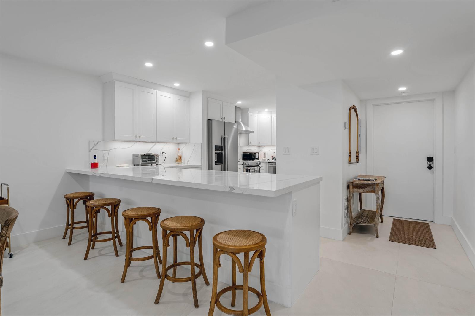 A white kitchen features a marble-topped breakfast bar with five wooden stools and recessed lighting — 401 Briny Avenue # 315, Pompano Beach FL 33062, POMPANO BEACH, FL