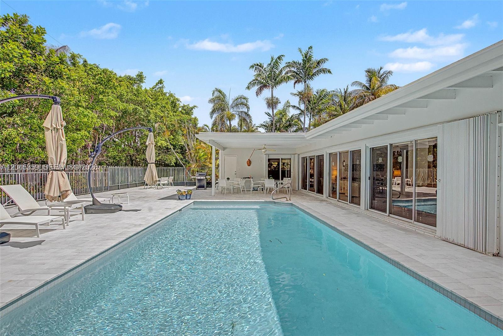 A rectangular swimming pool sits on a stone patio beside a modern white house — 340 Atlantic Rd, Key Biscayne FL 33149, KEY BISCAYNE, FL
