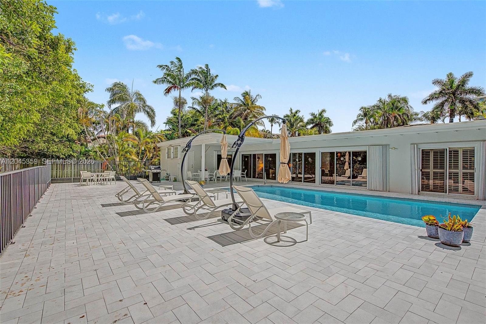 A swimming pool sits on a paved patio beside a white house with palm trees — 340 Atlantic Rd, Key Biscayne FL 33149, KEY BISCAYNE, FL