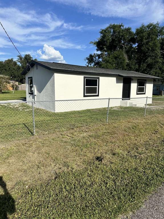 A single-story house with light-colored stucco walls and a dark roof behind a chain-link fence — 3329 LYNN DRIVE, LAKELAND, FL