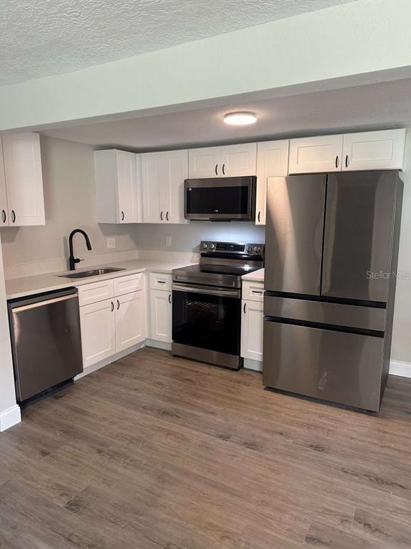 A kitchen features white cabinets, stainless steel appliances, a dark faucet, and wood-look flooring — 3329 LYNN DRIVE, LAKELAND, FL