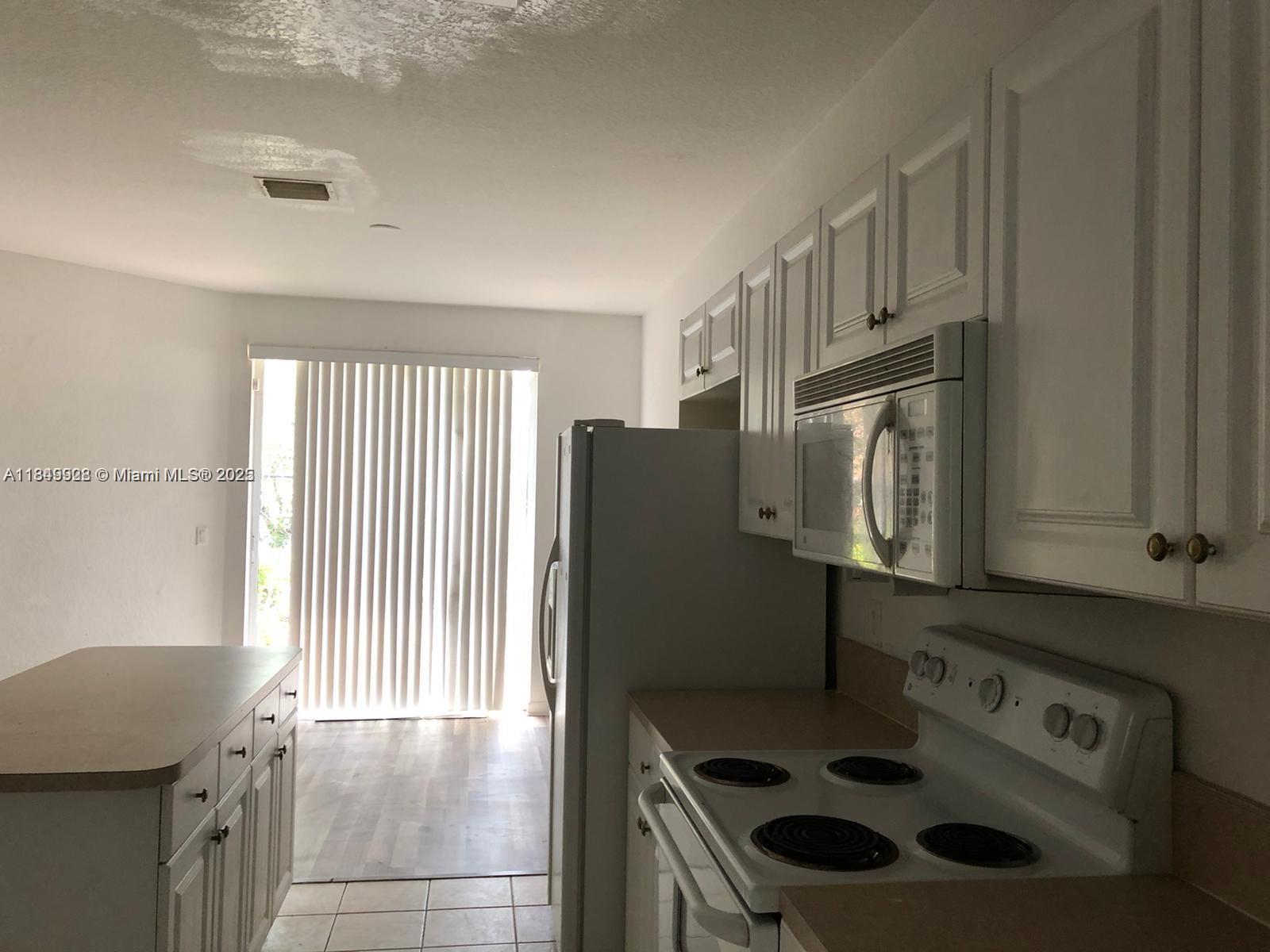 A kitchen features white cabinets, a white stove, a microwave, and a sliding glass door — 1911 Hibiscus Ln, Riviera Beach FL 33404, RIVIERA BEACH, FL