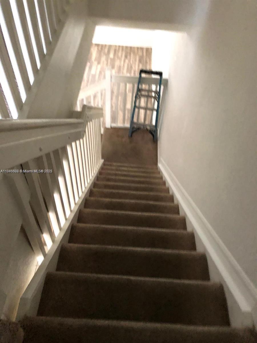 A carpeted staircase with white railings leads to a landing with a blue ladder — 1911 Hibiscus Ln, Riviera Beach FL 33404, RIVIERA BEACH, FL