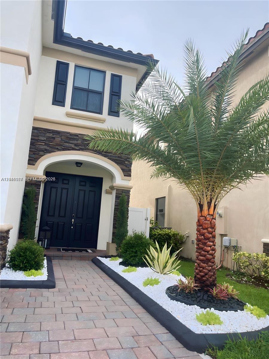 The exterior of a two-story home features a stone-accented entryway, black double doors, and landscaping — 8719 W 33rd Ave, Hialeah FL 33018, HIALEAH, FL
