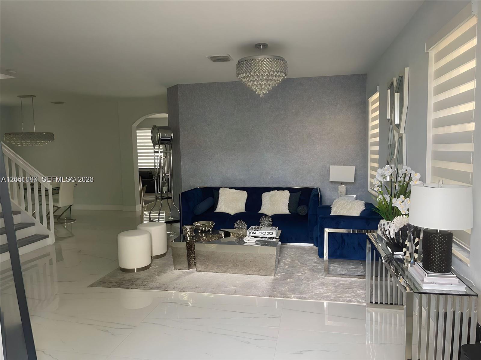 A living room features a blue velvet sofa, mirrored coffee tables, and a crystal chandelier — 8719 W 33rd Ave, Hialeah FL 33018, HIALEAH, FL