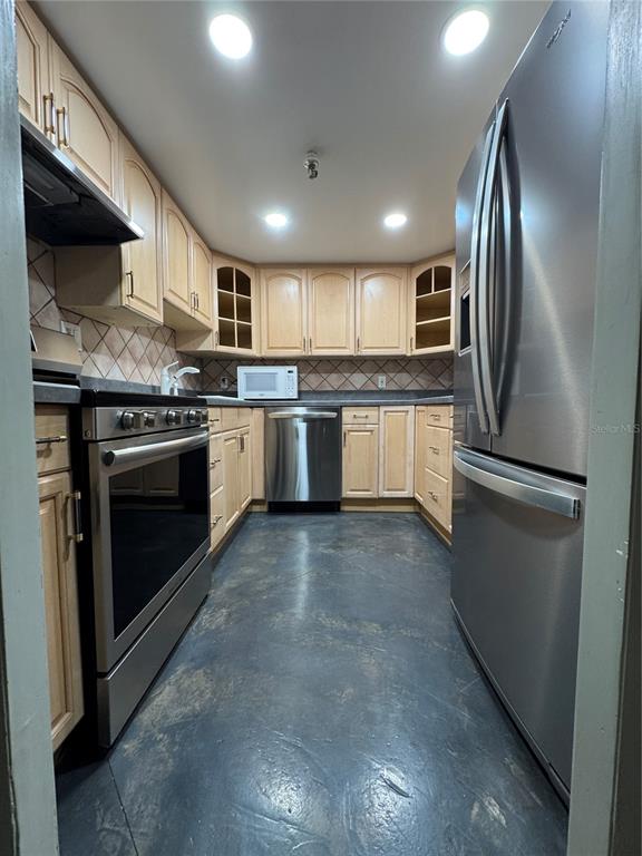 A galley kitchen features light wood cabinets, stainless steel appliances, and dark concrete flooring — 400 E COLONIAL DRIVE UNIT 108, ORLANDO, FL