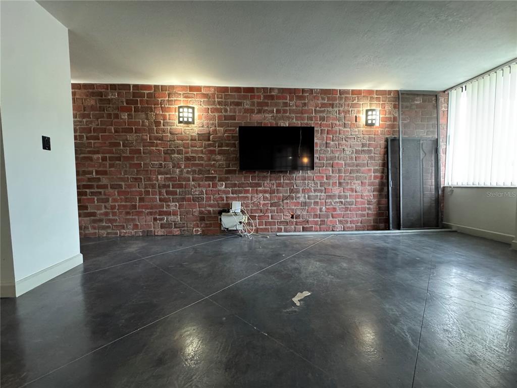 A living room features a red brick accent wall, a mounted television, and concrete flooring — 400 E COLONIAL DRIVE UNIT 108, ORLANDO, FL