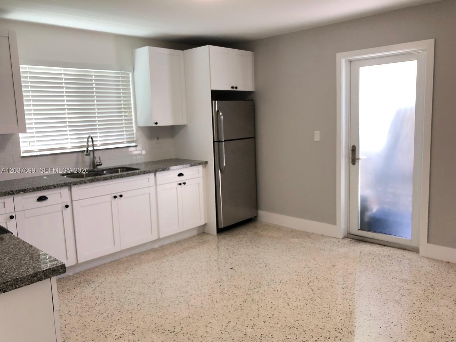 A kitchen features white cabinets, granite countertops, a stainless steel refrigerator, and terrazzo flooring — 12020 NE 12th Ct # 12020, Biscayne Park FL 33161, BISCAYNE PARK, FL