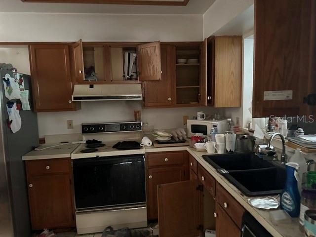A kitchen features wood cabinets, a black stove, a double sink, and a stainless refrigerator — 3977 MERMOOR DRIVE, PALM HARBOR, FL