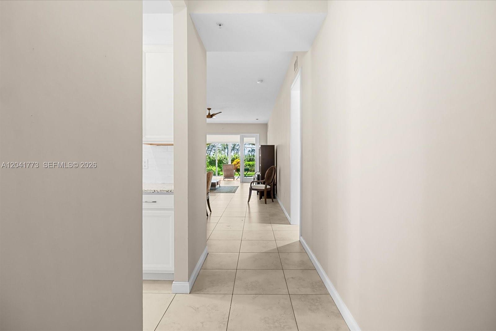A tiled hallway leads from a kitchen area toward a bright living room with glass doors — 38 E Harbour Isle Dr E # 104, Fort Pierce FL 34949, FORT PIERCE, FL