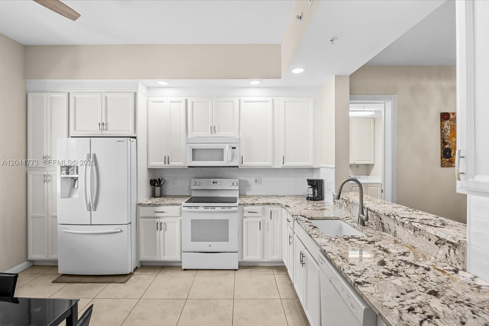 A kitchen features white cabinets, granite countertops, white appliances, and light-colored tile flooring — 38 E Harbour Isle Dr E # 104, Fort Pierce FL 34949, FORT PIERCE, FL