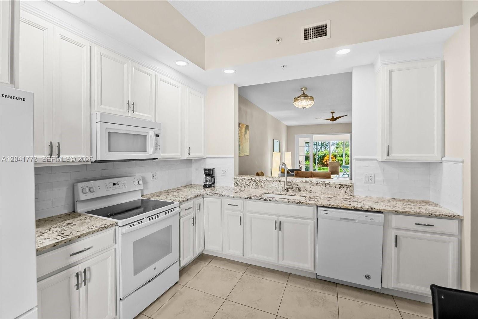 A white kitchen features granite countertops, stainless steel appliances, and an open pass-through window — 38 E Harbour Isle Dr E # 104, Fort Pierce FL 34949, FORT PIERCE, FL