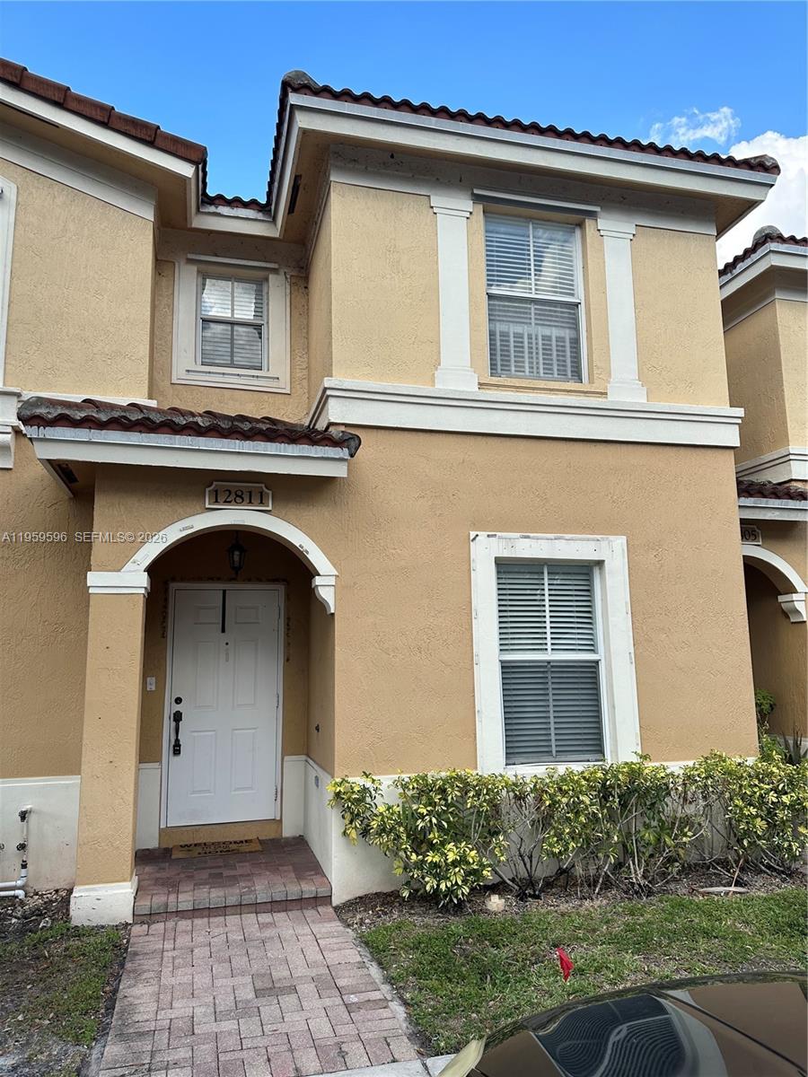 A two-story tan stucco townhouse features a white front door and a brick walkway — 12811 SW 30th St # 110, Miramar FL 33027, MIRAMAR, FL