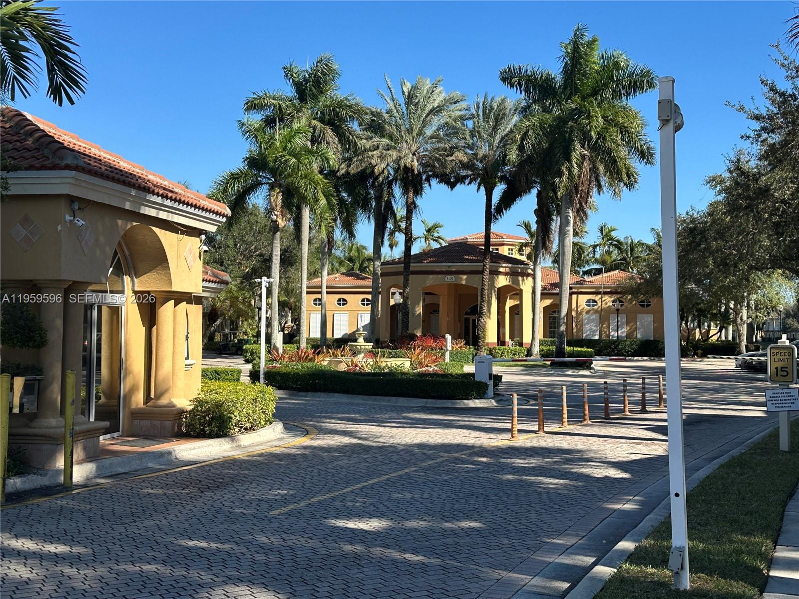 A paved driveway leads to a Mediterranean-style clubhouse entrance surrounded by palm trees and landscaping — 12811 SW 30th St # 110, Miramar FL 33027, MIRAMAR, FL