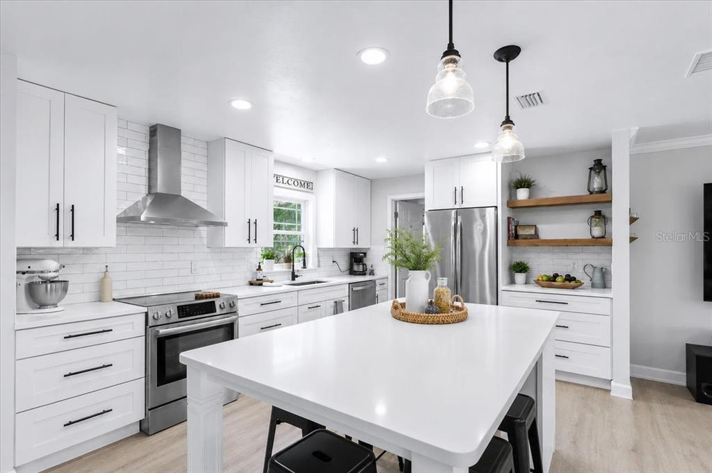 A bright, modern kitchen features white cabinetry, a central island, and stainless steel appliances — 3201 NW 202 STREET, NEWBERRY, FL