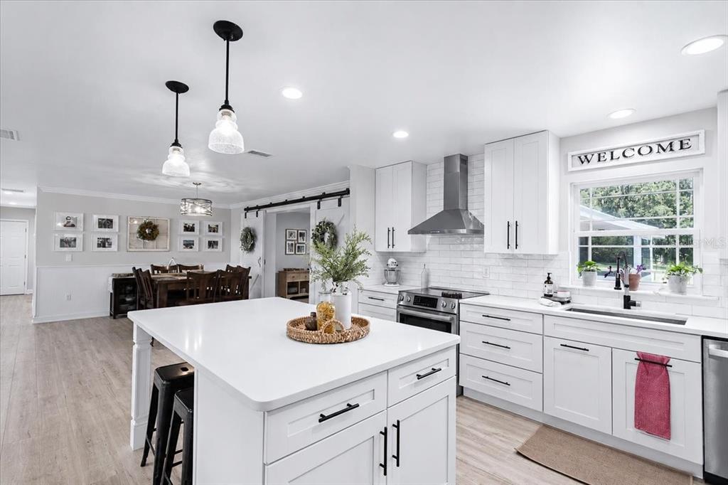 A modern white kitchen features a central island, stainless steel appliances, and light wood flooring — 3201 NW 202 STREET, NEWBERRY, FL