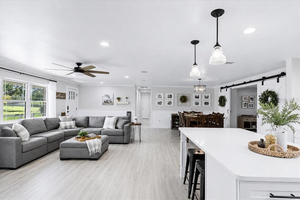 An open-concept living room and kitchen feature light wood flooring, a gray sectional, and island — 3201 NW 202 STREET, NEWBERRY, FL