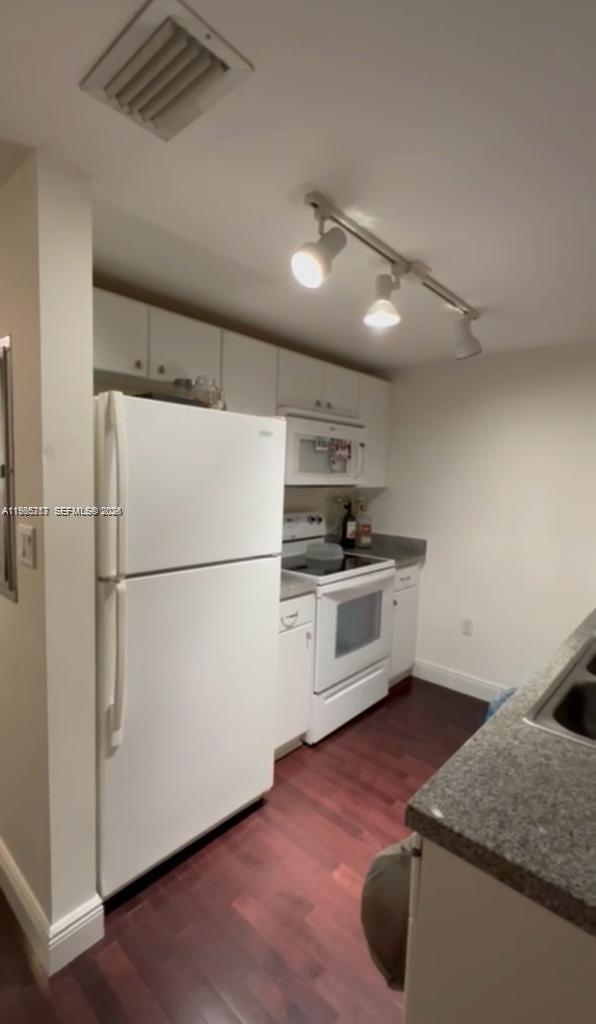 A kitchen features white cabinets, white appliances, dark wood flooring, and track lighting — 2740 SW 28th Ter # 503, Miami FL 33133, MIAMI, FL
