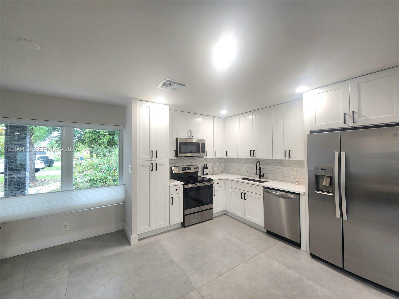 A modern kitchen features white cabinetry, stainless steel appliances, and large gray floor tiles — 141 NE 30th St, Wilton Manors FL 33334, WILTON MANORS, FL