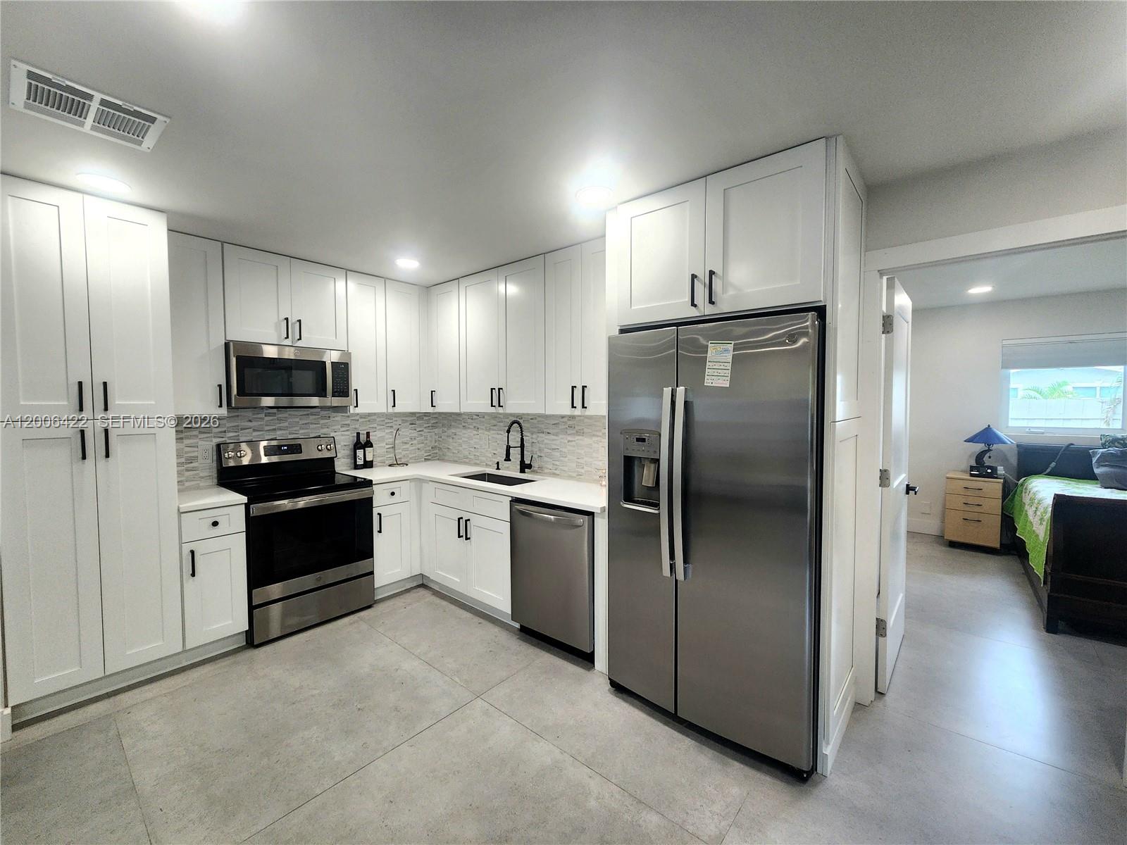 A modern kitchen features white cabinets, stainless steel appliances, and light gray tile flooring — 141 NE 30th St, Wilton Manors FL 33334, WILTON MANORS, FL