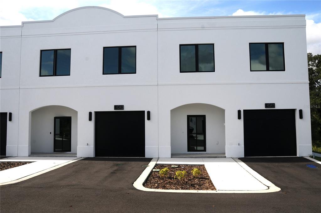A two-story white townhouse exterior features black garage doors, matching window frames, and arched entryways — 4341 CAMBIO GARDENS COURT, TAMPA, FL