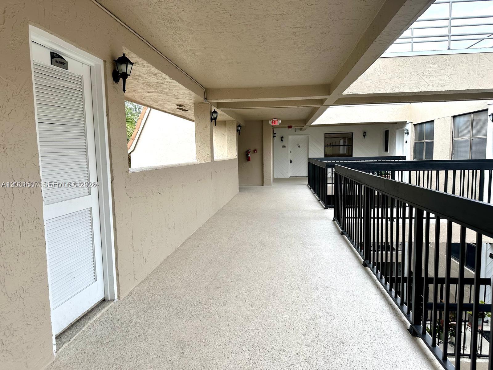 An outdoor apartment building walkway features a white louvered door, black railings, and beige walls — 601 Ives Dairy Rd # 8, Miami FL 33179, MIAMI, FL