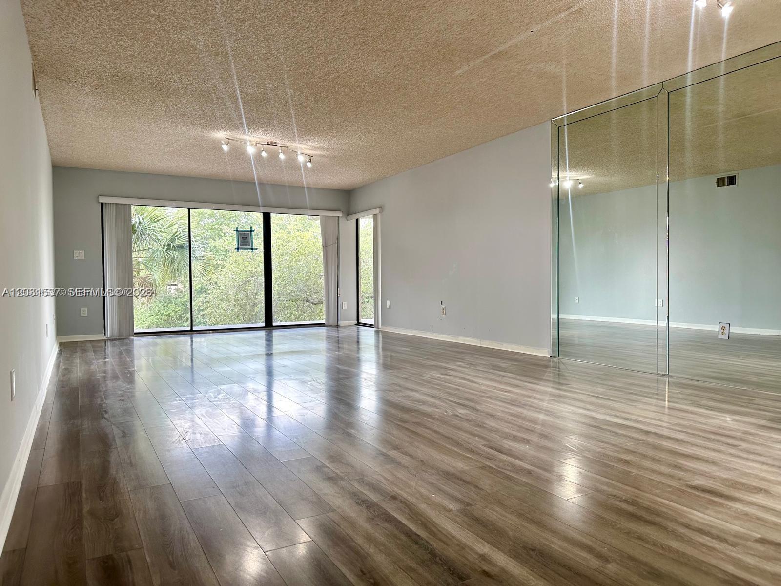 An empty living room features wood-look flooring, a popcorn ceiling, and a large mirrored wall — 601 Ives Dairy Rd # 8, Miami FL 33179, MIAMI, FL
