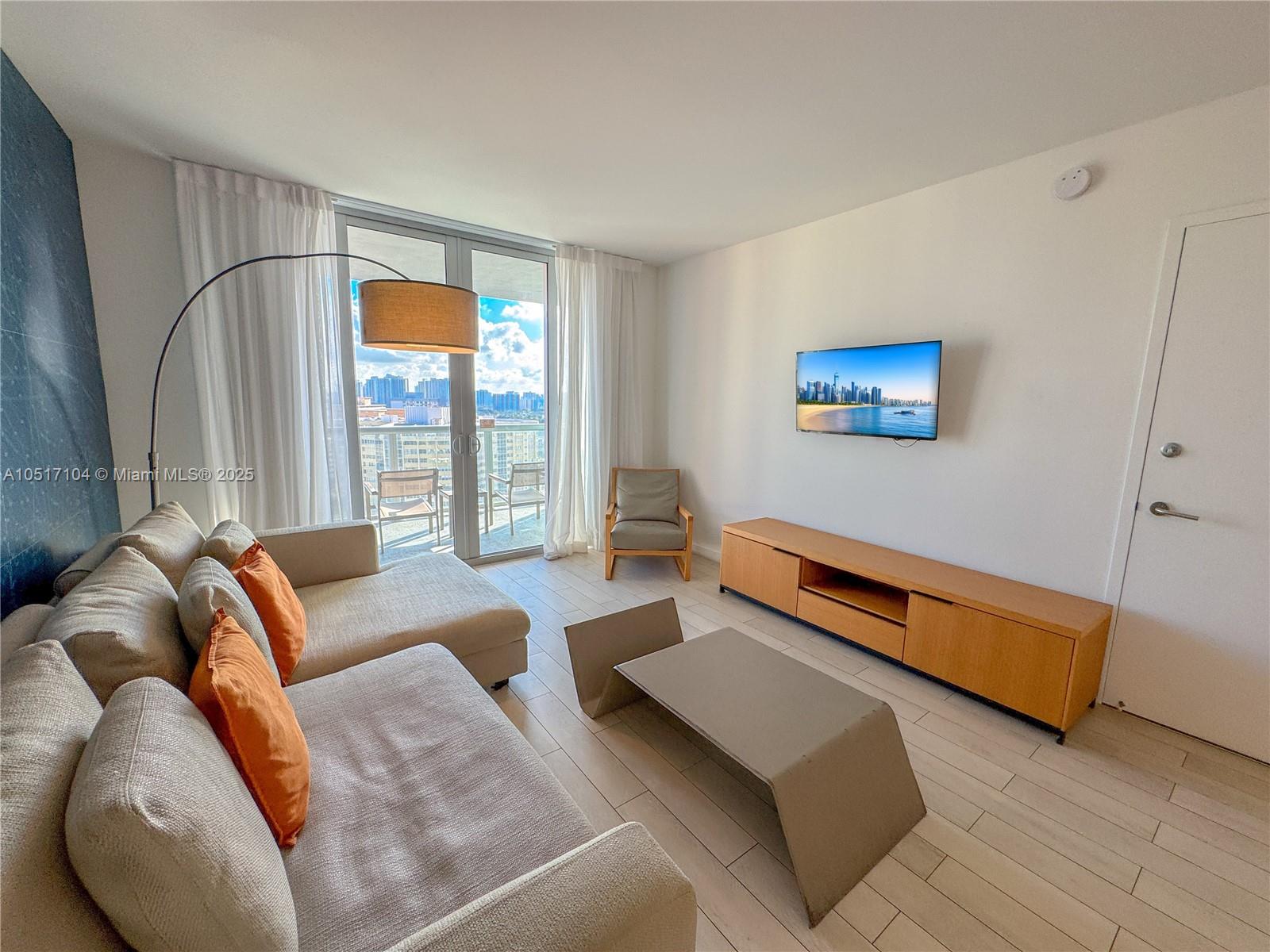 A living room features a beige sectional sofa, a wooden media console, and a balcony view — 2602 E Hallandale Beach Blvd # 1708, Hallandale Beach FL 33009, HALLANDALE BEACH, FL