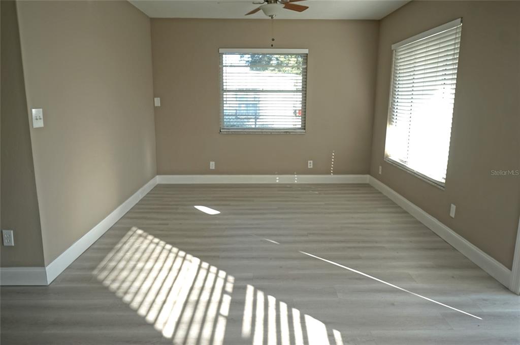 An empty room features light-colored wood-look flooring, beige walls, and two windows with blinds — 3519 W PRICE AVENUE, TAMPA, FL