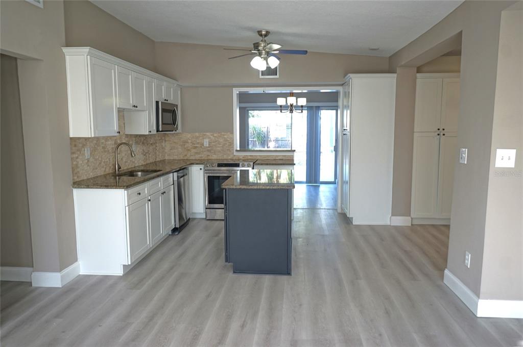 A kitchen features white cabinets, a dark gray island, granite countertops, and light wood flooring — 3519 W PRICE AVENUE, TAMPA, FL