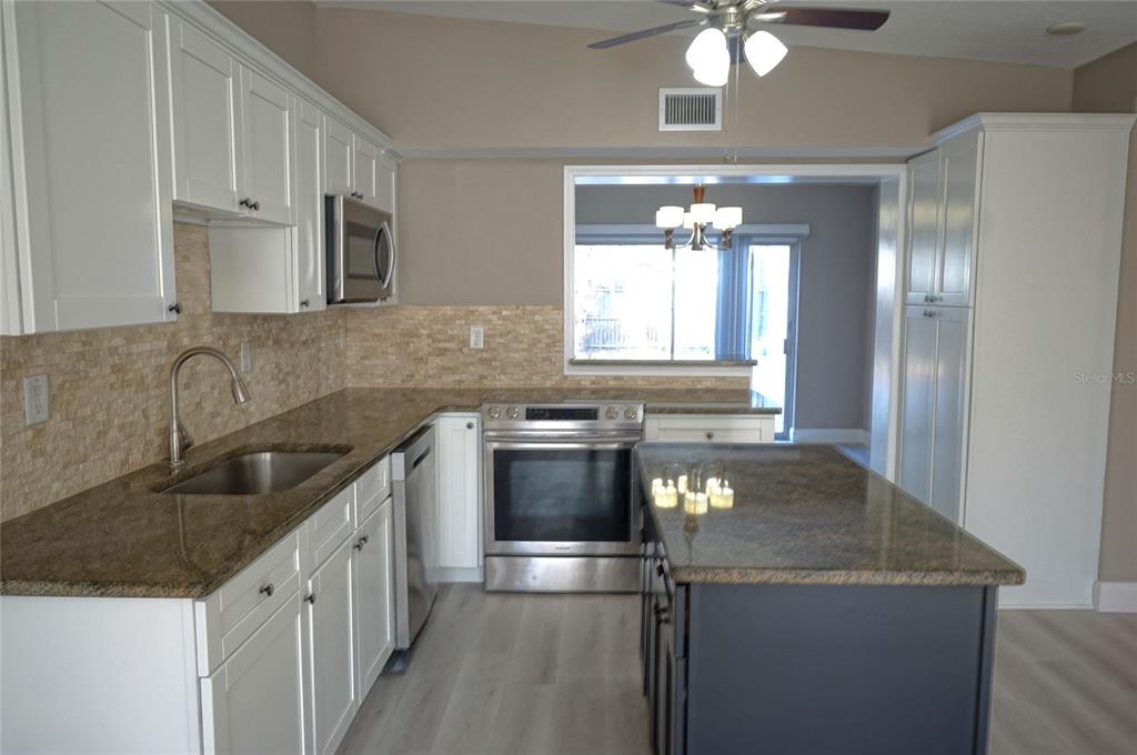 A kitchen features white cabinets, granite countertops, a center island, and stainless steel appliances — 3519 W PRICE AVENUE, TAMPA, FL