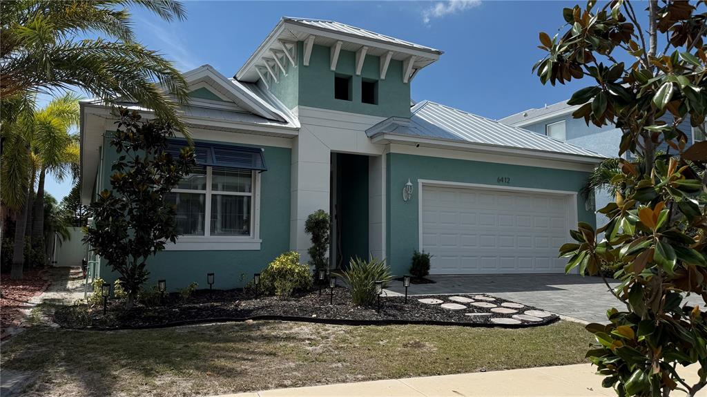 A teal, single-story house with a white garage and a metal roof under a blue sky — 6412 GRENADA ISLAND AVENUE, APOLLO BEACH, FL