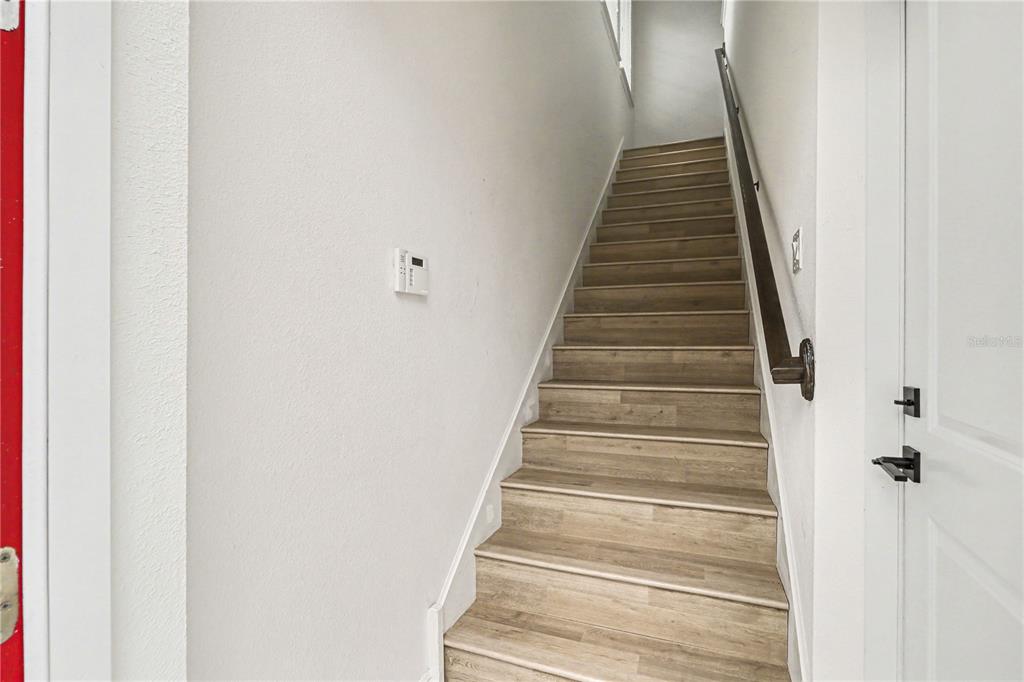 A staircase with wood-look flooring and a dark handrail leads to an upper level — 8274 R NEMOURS PARKWAY, ORLANDO, FL