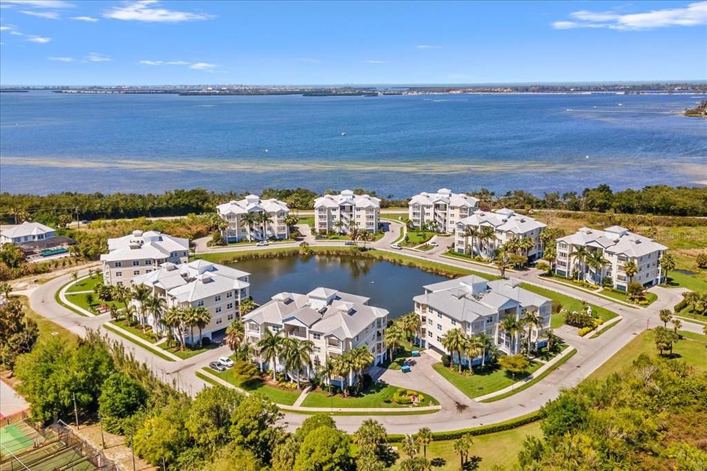 An aerial view of a residential complex with multiple buildings surrounding a central pond — 3418 79TH STREET CIRCLE W UNIT 303, BRADENTON, FL
