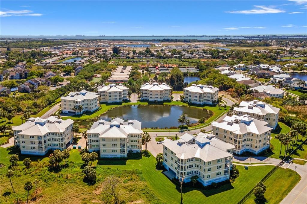 An aerial view shows several multi-story apartment buildings surrounding a central pond — 3418 79TH STREET CIRCLE W UNIT 303, BRADENTON, FL