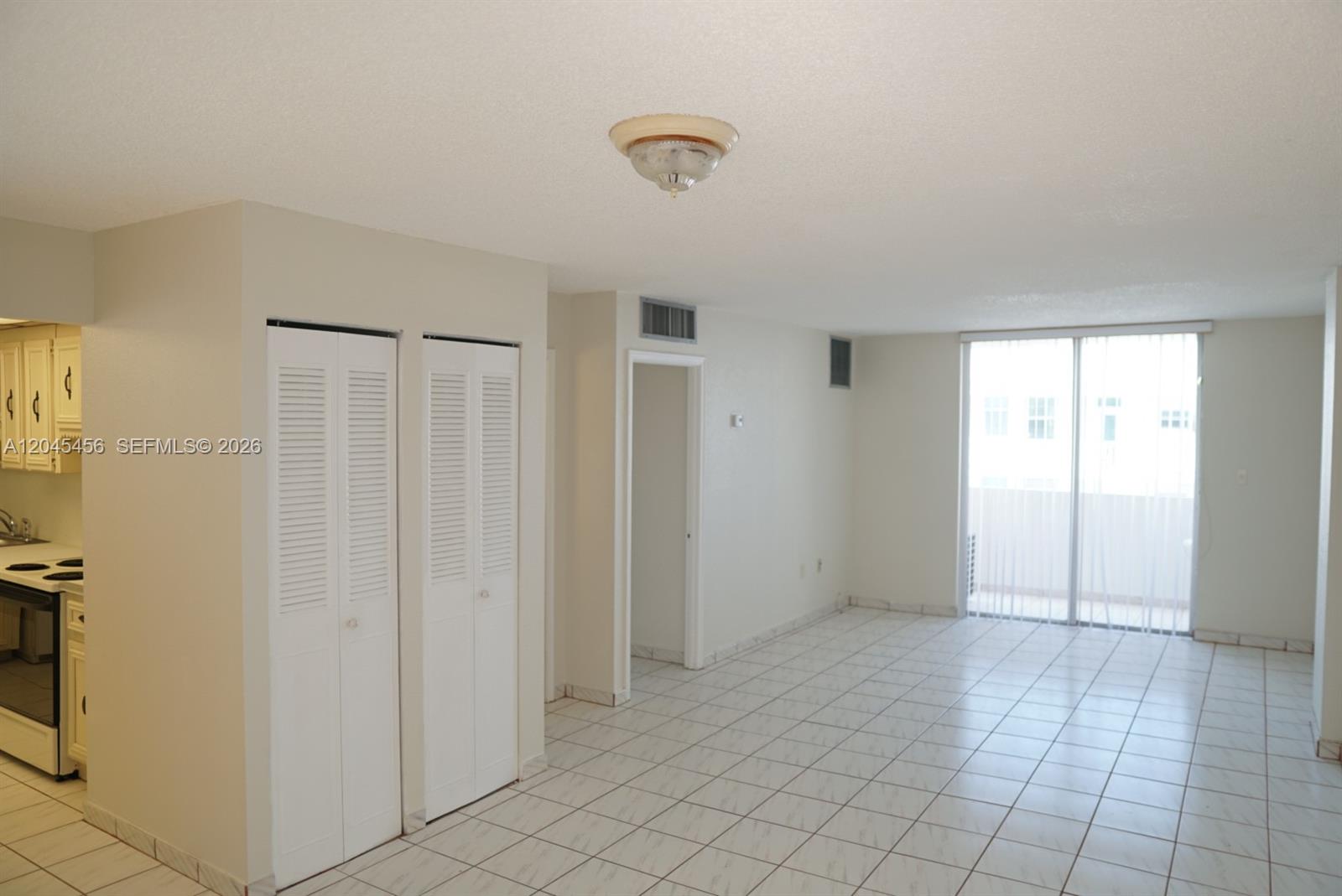 An empty room with white tile flooring, two louvered closet doors, and a sliding glass door — 1750 James Ave # 7K, Miami Beach FL 33139, MIAMI BEACH, FL