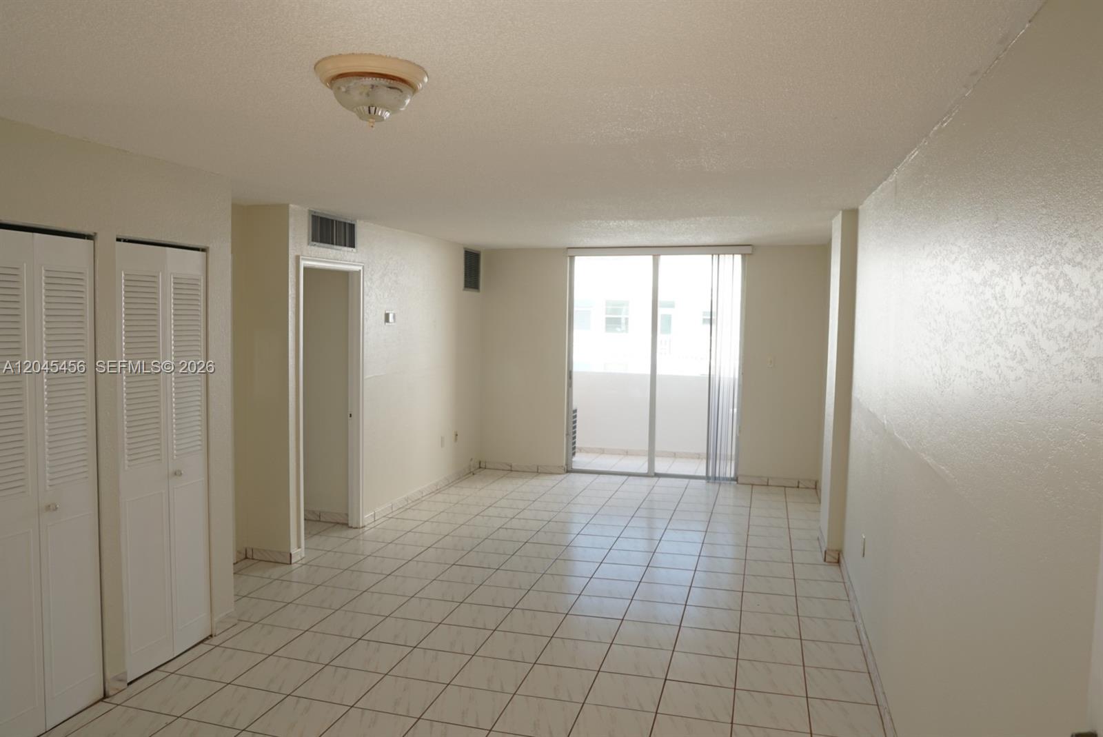 An empty room with white tile floors, a ceiling light, and sliding glass balcony doors — 1750 James Ave # 7K, Miami Beach FL 33139, MIAMI BEACH, FL