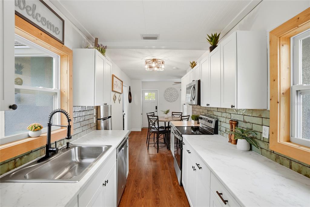 A galley kitchen features white cabinets, marble-look countertops, green subway tile backsplash, and wood flooring — 4627 1ST AVENUE N, ST PETERSBURG, FL