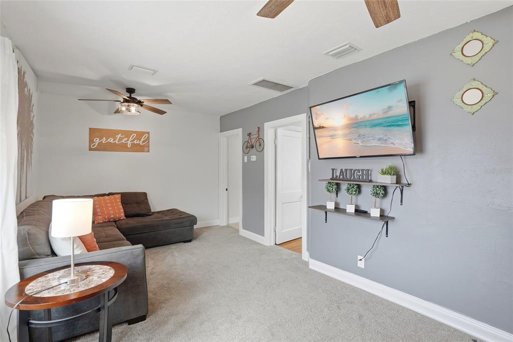 A living room features gray carpet, a sectional sofa, a wall-mounted television, and shelving — 4627 1ST AVENUE N, ST PETERSBURG, FL