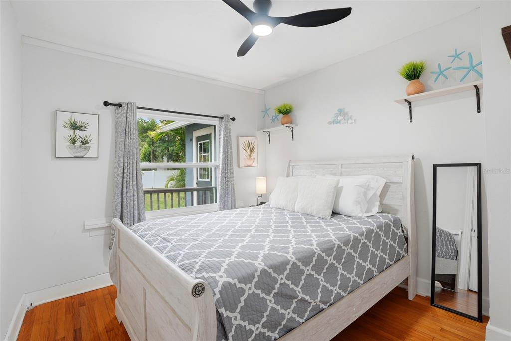 A bedroom features a white bed, hardwood floors, a ceiling fan, and wall-mounted shelves — 4627 1ST AVENUE N, ST PETERSBURG, FL