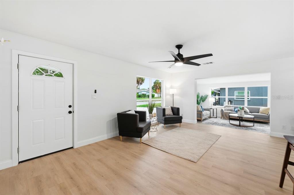 A bright living room features light wood flooring, a ceiling fan, and a front door — 6324 CASE AVENUE, BRADENTON, FL