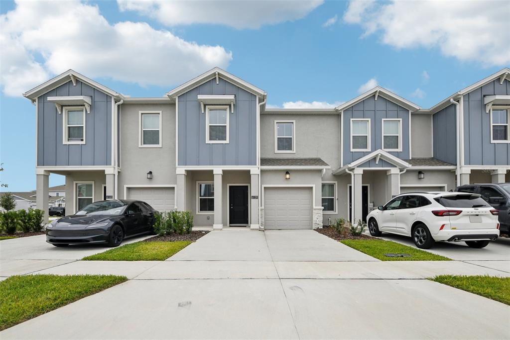 A row of modern two-story townhouses with blue siding, gray stucco, and attached garages — 6159 PEACEFUL PARK WAY, CLERMONT, FL