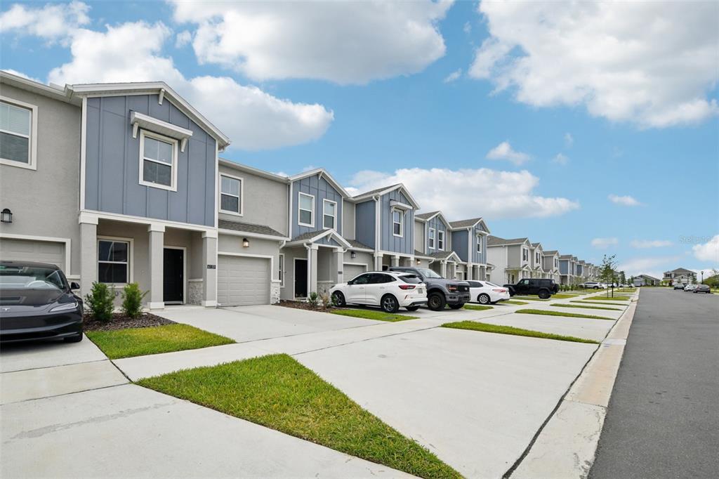 A row of modern two-story townhomes with attached garages and driveways under a blue sky — 6159 PEACEFUL PARK WAY, CLERMONT, FL