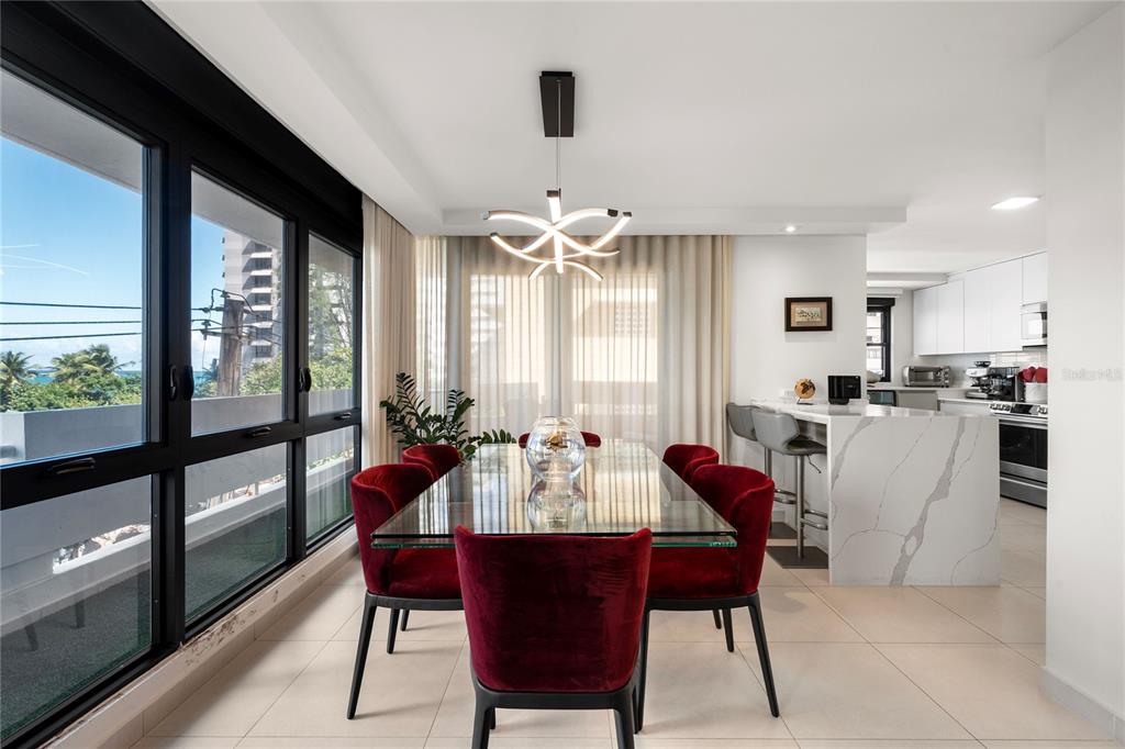 A dining room features a glass table, red velvet chairs, and large windows overlooking the ocean — 1510 ASHFORD AVENUE UNIT 3, SAN JUAN, PR