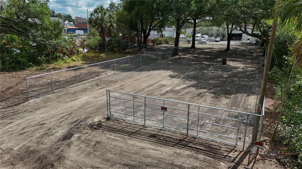 A fenced, dirt-covered vacant lot is surrounded by trees and adjacent to a parking area — 208 S FRANKLIN STREET, PLANT CITY, FL