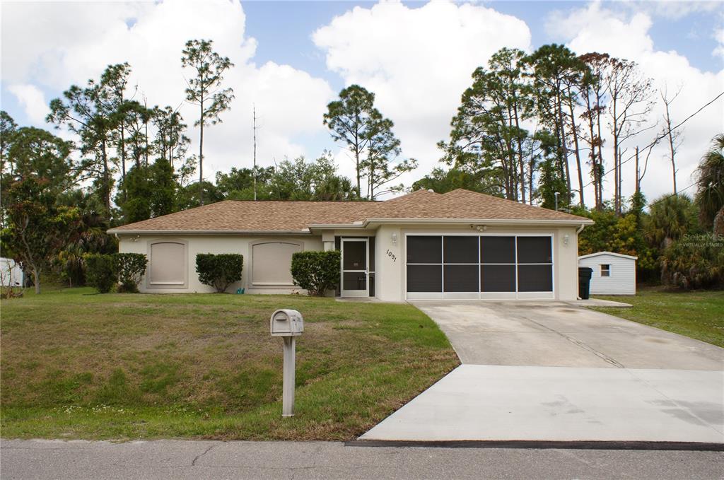 A single-story house with a tan exterior, a brown shingled roof, and a concrete driveway — 1091 LUAU STREET, NORTH PORT, FL