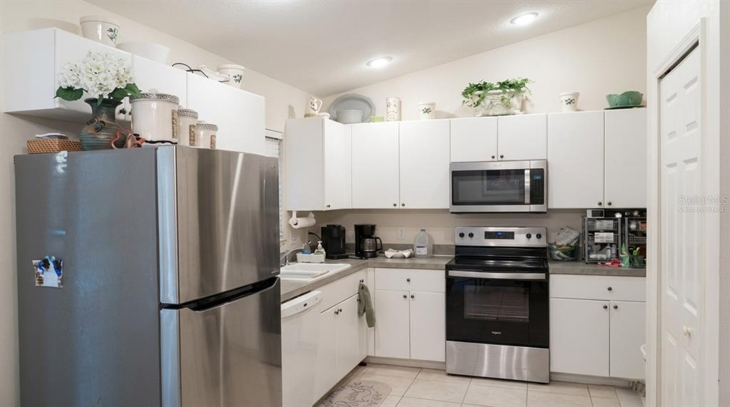 A kitchen features white cabinets, stainless steel appliances, and light-colored tile flooring — 1091 LUAU STREET, NORTH PORT, FL