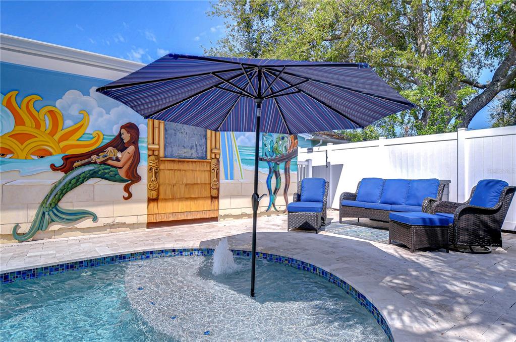 A patio features a pool with a fountain, a striped umbrella, and blue wicker furniture — 1922 55TH STREET S, GULFPORT, FL